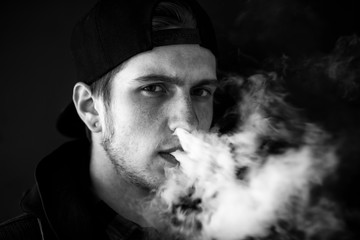 Vape teenager. Portrait of young handsome guy in a cap smoking an electronic cigarette on the...