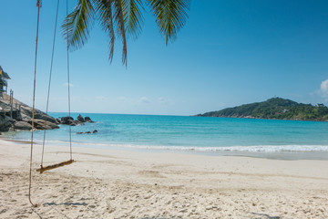 Empty wooden swing on an exotic beach - Phangan island, Thailand. Wodden swing tied with ropes to a tree with sea and beach in the background.