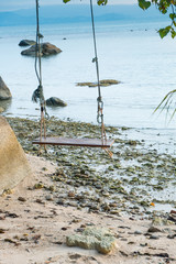 Empty wooden swing on an exotic beach - Phangan island, Thailand. Wodden swing tied with ropes to a tree with sea in the background.