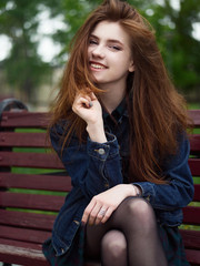 Emotional portrait of naturally beautiful redhead young hipster woman in stylish jeans jacket, plaid skirt, black tights looking into camera playing with hair enjoying her free time on cloudy day with