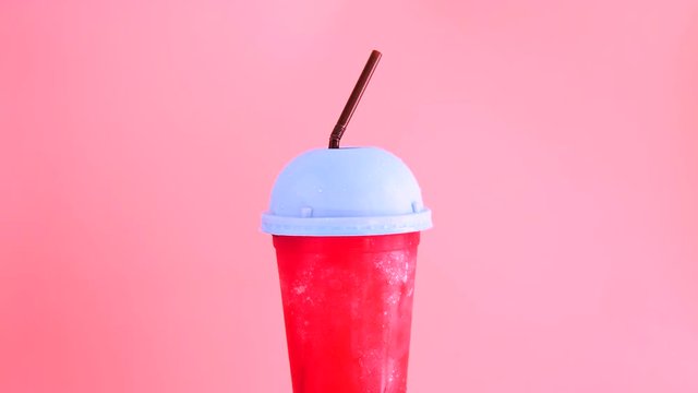 Red liquid drink in plastic cup rotating with color background.