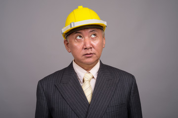 Mature Asian construction businessman against gray background