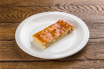 Homemade pie with potatoes on white plate isolated on wooden background