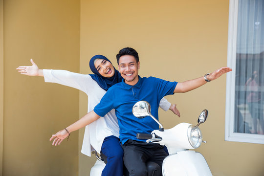 happy asian muslim couple riding motorcyle or scooter