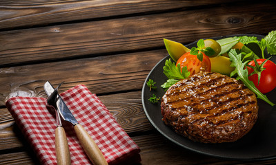 Fried fresh large beef burger cutlet with salad and herbs on black plate on wooden table