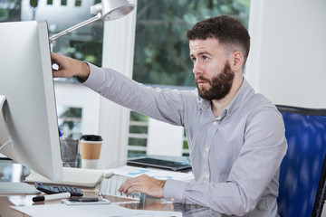 Bearded confident businessman sitting at the workplace and pointing at computer monitor while working over business presentation at office