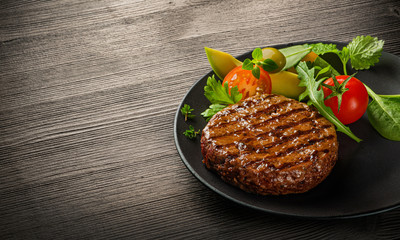 Fried fresh large beef burger with salad and herbs on black plate on wooden table