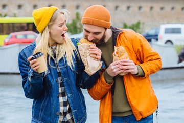 Hungry beard man taking croissants out of woman and biting it with greed at city street. I dont...