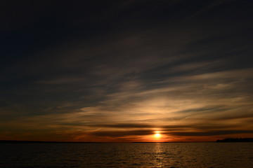 Sky a bright circle of the sun in the sunset glows in the clouds above the water of the lake