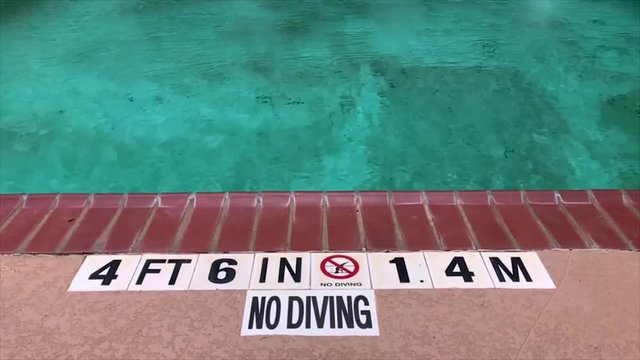 Edge of a pool with a no diving sign. Shallow water public pool with slow motion water ripples.