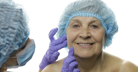 Smiling elderly female in protective hat. Plastic surgeon checking woman face