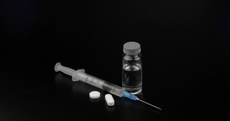 Pills, syringe and ampoule with vaccination on black background