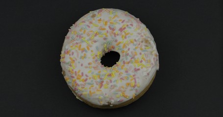 Sweet donut on black background. Top view. Tasty, fresh sprinkled donut