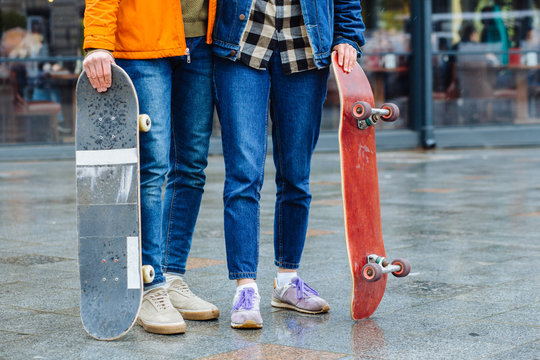 Close up feet of a girl in old sneakers and longboard standing in the street at city outdoor in spring rainy day. Active Sport, fitness lifestyle concept. Urban scene, city life.