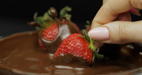 Hand dipping strawberry in melted chocolate. Fresh berries sweet dessert food