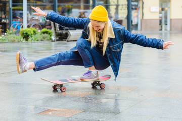 Full body of happy sporty blond hipster woman in yellow hat and blue denim jacket balancing on...