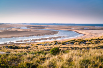 Fototapeta na wymiar Budle Water meanders to the North Sea, the mud flats at Budle Bay at low tide are part of Lindisfarne Nature reserve on Northumberland's AONB coastline