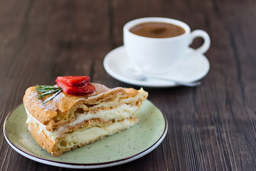 A piece of cake handmade with custard and a cup of coffee on a brown table.