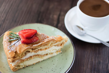 A piece of cake handmade with custard and a cup of coffee on a brown table.
