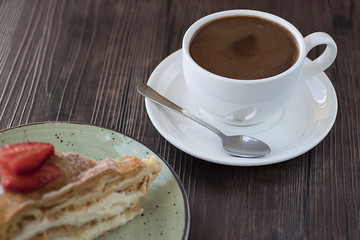 A piece of cake handmade with custard and a cup of coffee on a brown table.