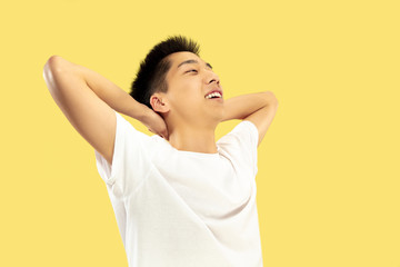 Korean young man's half-length portrait on yellow studio background. Male model in white shirt. Resting and smiling. Concept of human emotions, facial expression. Front view. Trendy colors.