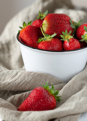Strawberries with tails in a pot on a gray cloth.
