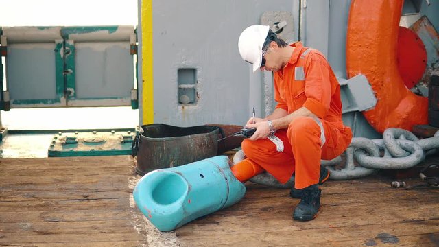 Marine chief officer or chief mate on deck of ship or vessel. He fills up ahts vessel checklist. Ship routine paperwork. He holds VHF walkie-talkie radio in hands.
