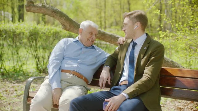 Young man is smiling to his senior farher on meeting in the park on summer day