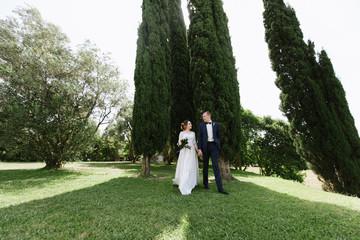 The groom in a suit and the bride in a wedding dress are walking in the park