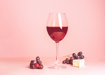 A glass with red wine and snack on a delicate pink background. Selective focus. Copy space. Minimalism