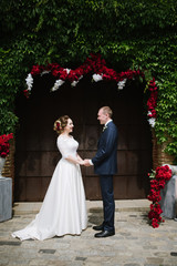 The groom in a suit and the bride in a wedding dress are standing at the wedding arch at the wedding ceremony