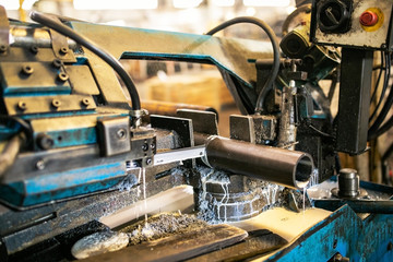 Automatic band saw machine cutting raw steel rods. The band saw machine cutting raw metals rods the with the coolant fluid.The industrial sawing machine cutting the material rod.