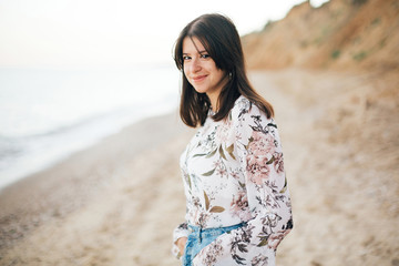 Stylish hipster girl walking on beach at sea. Calm portrait of happy fashionable boho woman...