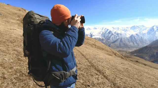 Portrait of a happy bearded traveler photographer in sunglasses and a hat with a reflex camera in his hands and taking pictures against the background of the mountains. Photo travel concept