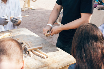 Wooden workshop. Hands carving spoon from wood, working with chisel close up. Process of making wooden spoon, chisel and shavings on dirty table. Handmade festival in summer park