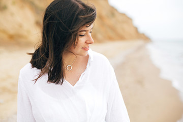 Stylish hipster girl relaxing on beach. Summer vacation. Portrait of  happy boho woman enjoying time and smiling at windy sea. Space for text. Calm moment.