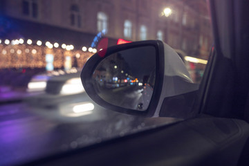 inside view of a taxi traveling through the city at night, windows lit with colorful lights, the facades of buildings are decorated with garlands