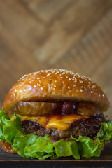 Burger, hamburger sandwich with cutlet of minced meat, melted cheese, berry cherry and pear. Side view on a wooden backdrop and light wooden board.