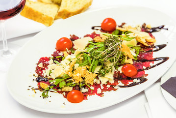 Snack on a white dish. Carpaccio, Parmesan, Arugula and Cherry Tomatoes