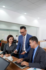 Businessman showing online document on digital tablet to his partners and they discussing it together in team at office