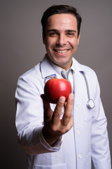 Handsome Persian man doctor against gray background