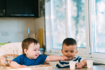 Children brother and sister in the kitchen eating yogurt on their own