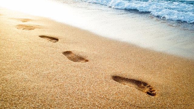 Closeup beautiful image of human footprints on wet sand at sea beach against beautiful sunset over the water surface