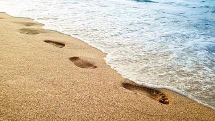 Closeup beautiful image of human footprints on wet sand at sea beach against beautiful sunset over the water surface
