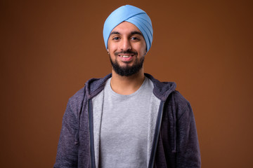 Young bearded Indian Sikh man wearing turban against brown backg
