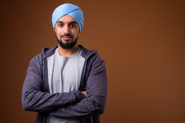 Young bearded Indian Sikh man wearing turban against brown backg