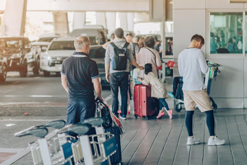 Passengers with big roller luggage stand to wait for the car to pick up at airport arrival terminal.
