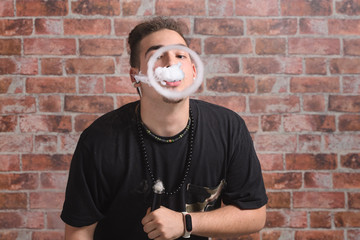 Vaper Smoke outdoor electronic cigarette near the brick wall. Young man smoking big cloud of steam