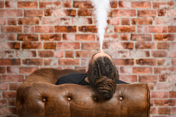 Vaper Smoke outdoor electronic cigarette near the brick wall. Young man smoking big cloud of steam