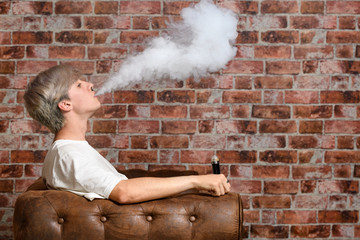 Vaper Smoke outdoor electronic cigarette near the brick wall. Young man smoking big cloud of steam